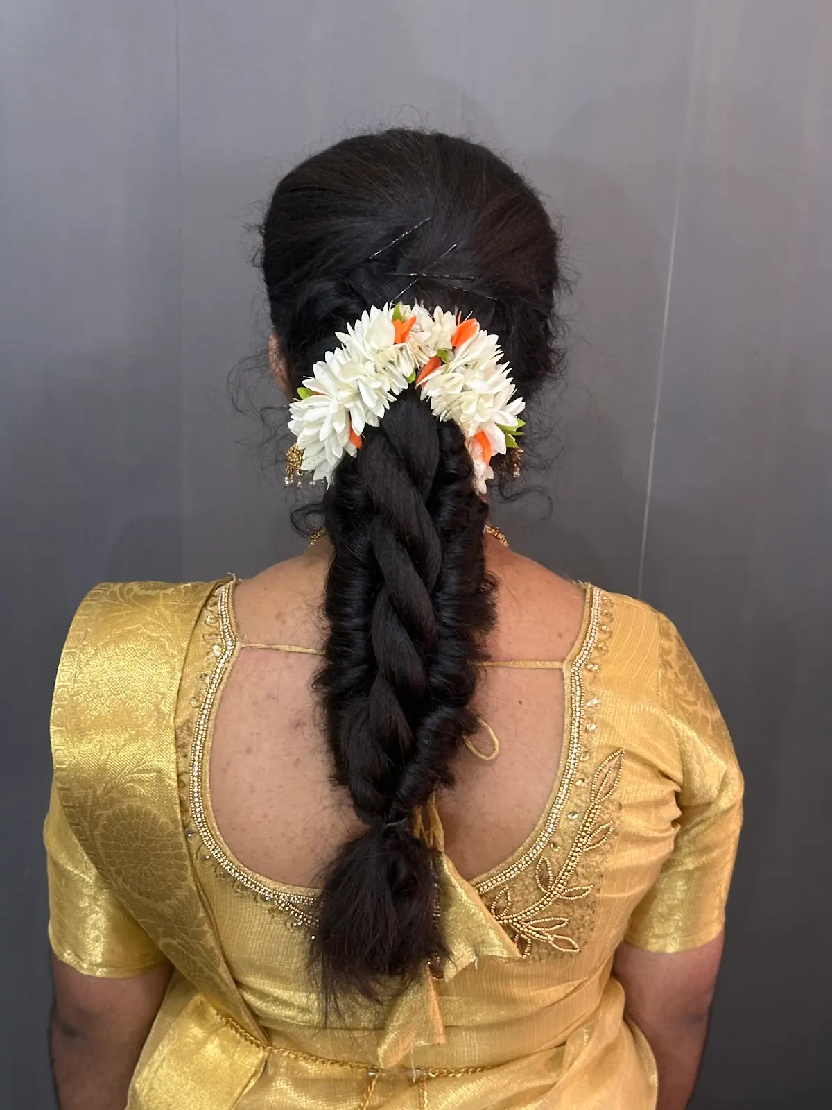 A bridal braid dressed with jasmine, seen from behind, against a gold blouse